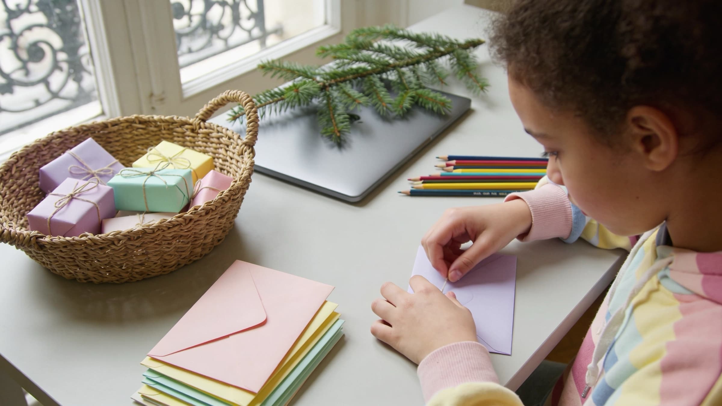 Bureau en décembre : panier de petits cadeaux emballés de papier pastel, enveloppes scellées et branche de sapin