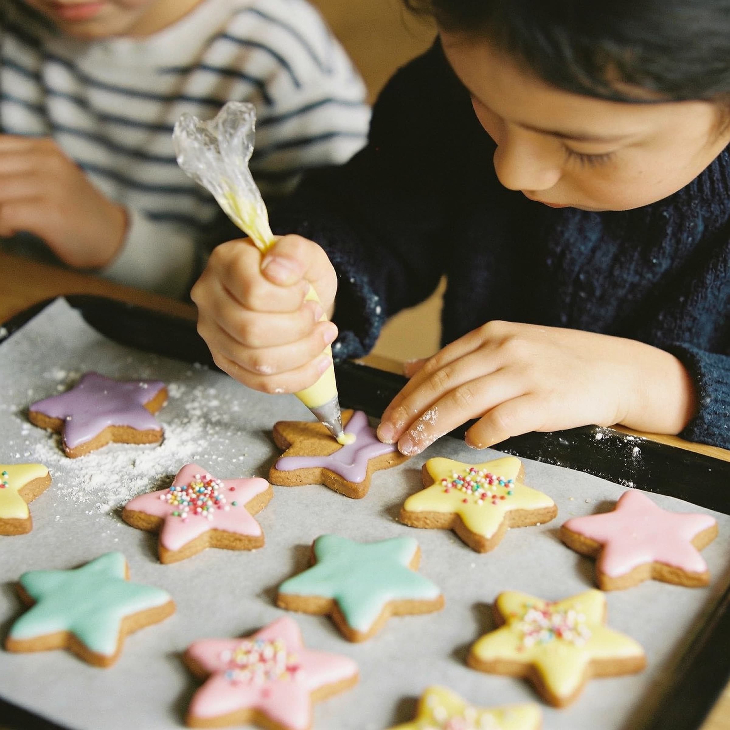 Enfants décorant des biscuits en étoile avec un glaçage pastel